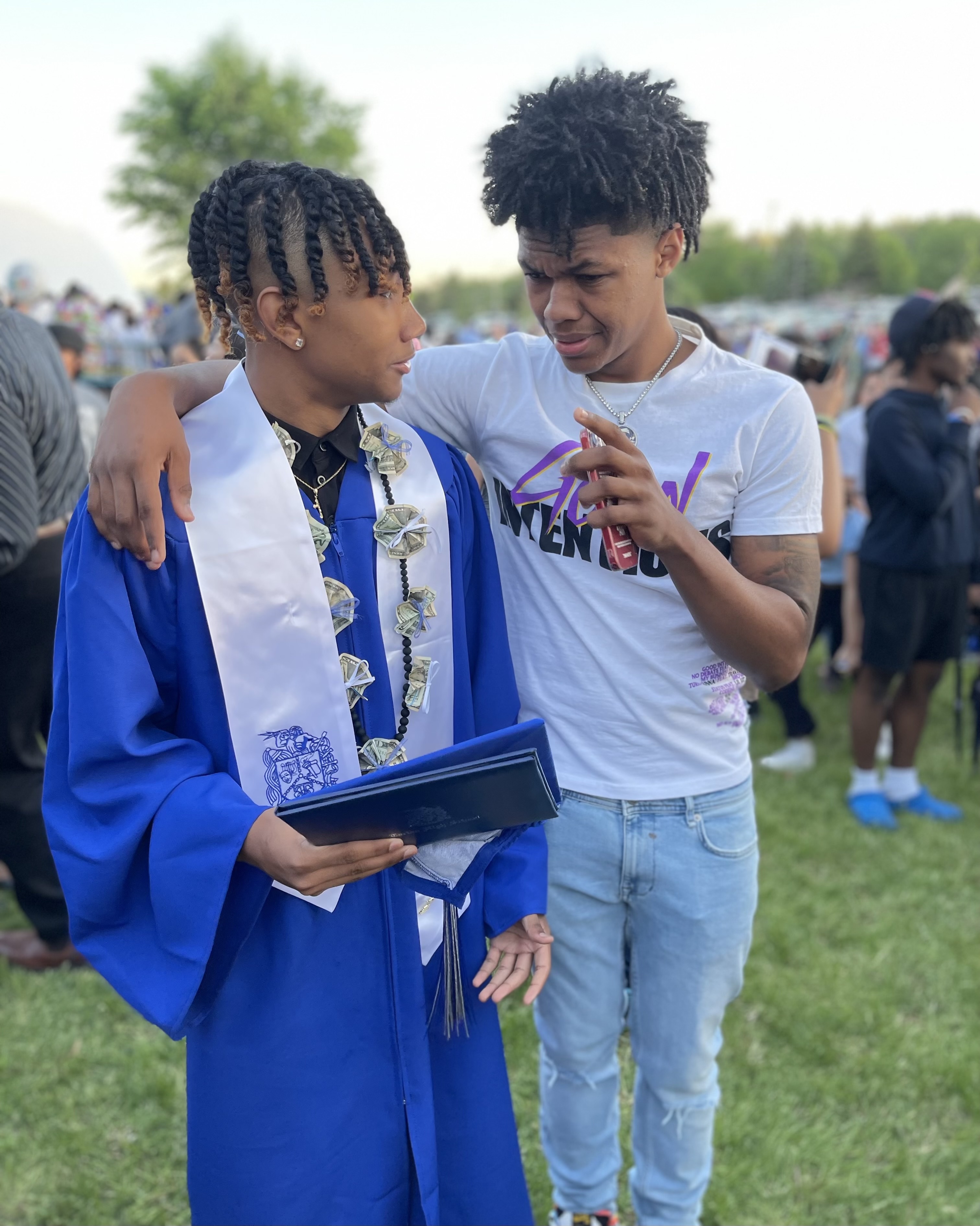 Graduate in blue cap and gown celebrating with a friend